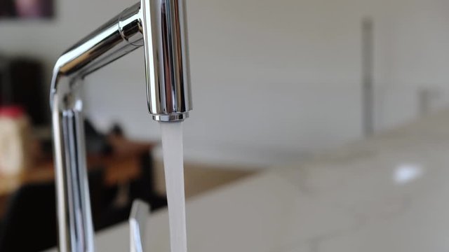 Closeup of chrome faucet in modern kitchen with caucasian woman hand opening and closing water