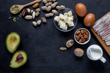 Keto product on black background: bacon, butter, nuts, cream, eggs, avocado. 