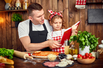 Girl wearing checkered apron reading red recipes book while father spreading sauce by dough for pizza in stylish wooden kitchen