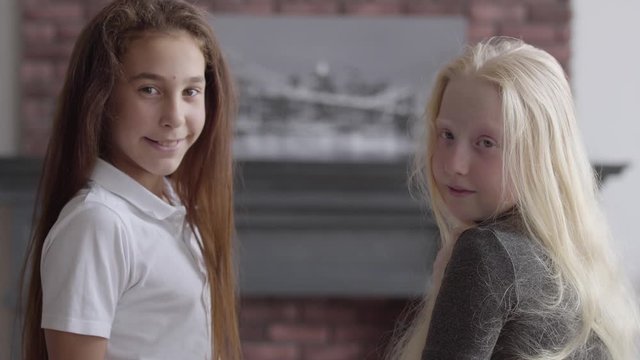 Portrait of brunette girl and albino girl with long hair waving hands looking at the camera smiling. Concept of friendship. Carefree childhood. Real people series.