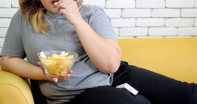 Fat woman eating potato chips on sofa and watching TV at home