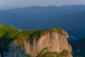 Camping on top of the mountain. A person can be seen on the edge of the cliff and her tent installed a few feet away.