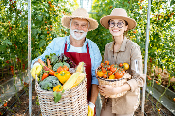 Portrait of a young woman with grandfather holding baskets full of fresh vegetable harvest in the...