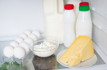 on a shelf in a white refrigerator, animal products, cream, milk, kefir, eggs, cottage cheese and cheese, and vegetables in a box