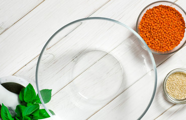 Glass plates with red lentils, sesame seeds and a large glass plate stand on wooden table