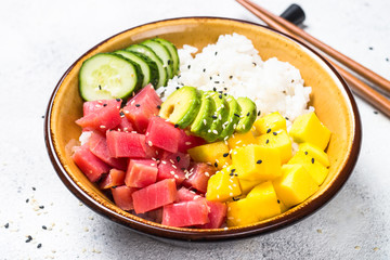 Tuna poke bowl with rice, avocado, mango and cucumber on white table.
