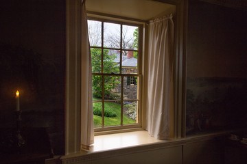 View  of landscape with brick house  through the old window. Mystic indow with curtains and candle