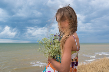 Portrait of a sad girl with flowers against the sea and cloudy sky