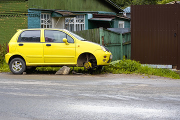 Yellow passenger car without a front wheel on the side of a country road. A car without a wheel on...
