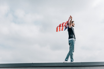 side view of handsome man in jeans and t-shirt holding american flag