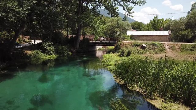 Drone clip flying forward just above the crystal clear moving river Tirino in the Abruzzo region in Italy. Passing through trees and facing an old building.