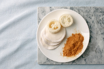 Eco friendly products for home cleaning, zero waste lifestyle, flat lay on white background. Mustard and natural luffa sponge on white plate, stylish minimalism