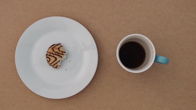 A stop motion animation overhead shot of coconut cookies on a plate being eaten bite by bite and a cup of coffee being drank.
