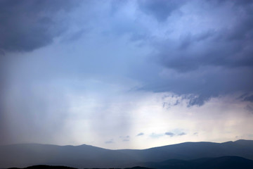 Naklejka na ściany i meble the rain from the clouds gradually covers the mountains.
