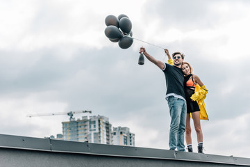 attractive woman holding black balloons and handsome man holding bottle