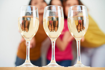 Close-up of three flutes full of champagne are on the table with three girls standing in the background