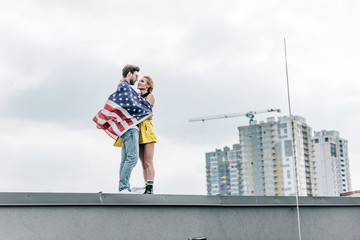 attractive woman and handsome man with american flag hugging on roof