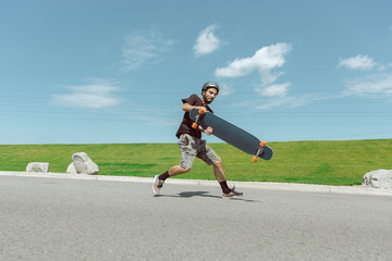 Obraz premium Skateboarder doing a trick at the city's street in sunny day. Young man in equipment riding and longboarding near by meadow in action. Concept of leisure activity, sport, extreme, hobby and motion.
