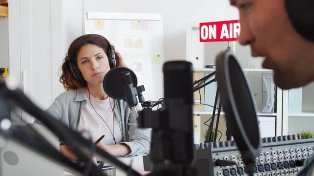 Ginger female radio host sitting at mike and having interview with male guest sitting in front of her