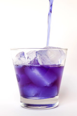 Pouring butterfly pea juice on ice in transparent glass isolated on white background 