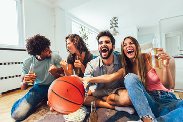 Happy friends or basketball fans watching basketball game on tv and celebrating victory at...