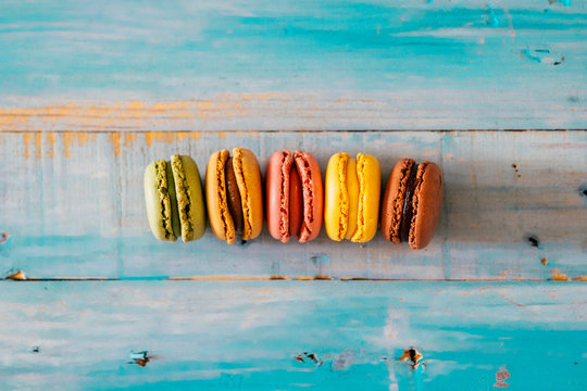 Coloured macarones biscuits on a blue wooden table background - concept of bakery and party lifestyle with sweet snacks - food decorations viewed from above with creak and chocolate