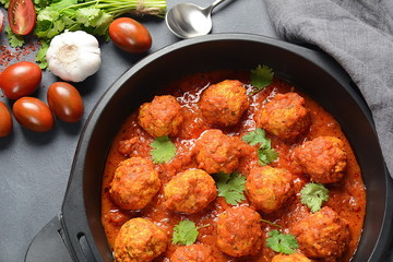 Meatballs in sweet and sour tomato sauce with spices served in a frying pan on dark background . Top view