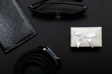 White gift box and a leather belt with a couple on black background, top view. 