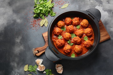 Meatballs in sweet and sour tomato sauce with spices served in a frying pan on dark background . Top view
