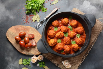 Meatballs in sweet and sour tomato sauce with spices served in a frying pan on dark background . Top view