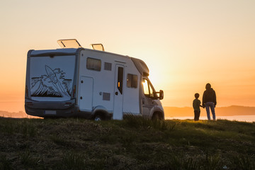 mother and son watching the sunset with their motor home at the edge of the sea - obrazy, fototapety, plakaty