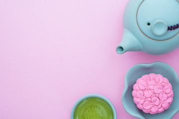 Pink mooncake, blue teapot, cup of green tea on a pink background. Chinese mid-autumn festival food.