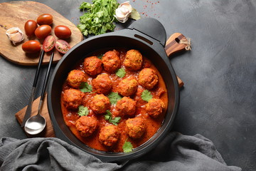 Meatballs in sweet and sour tomato sauce with spices served in a frying pan on dark background . Top view