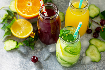 Various refreshments drinks - detox cucumber water, cherry juice and orange juice on stone table.