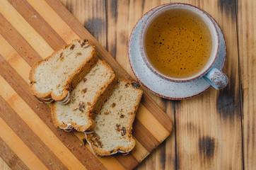 Breakfast with tea cup and pastries sliced on wooden board on a table. Top view