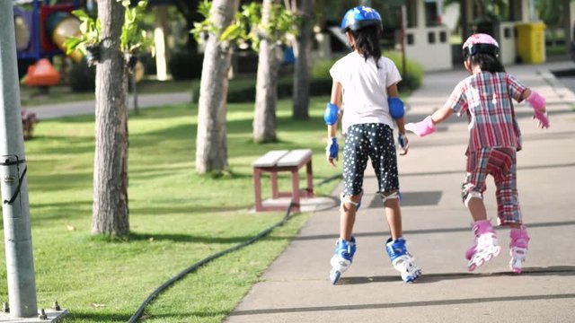 Back of children playing roller skating together in the park outdoor, slow motion.