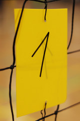 Number One written by black marker on yellow plastic card holds on volleyball net. Number used to identify courts in sports hall