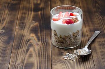 Healthy breakfast. Glass yogurt, fresh strawberry,  spoon with the scattered granule on a wooden table. Copyspace