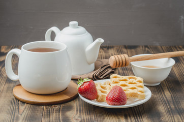 Delicious breakfast with tea, honey and wafers decorated with fresh strawberry on a wwoden table.