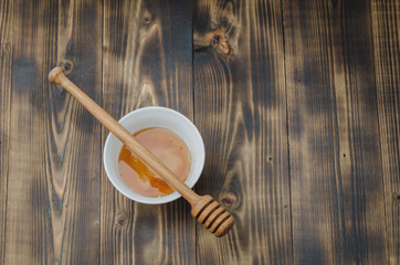 dipper on a white bowl with honey, wooden table. Top view, copyspace