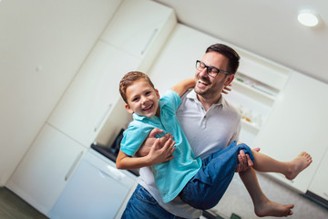 Fototapeta premium Image of satisfied smiling man piggybacking his son while having fun in modern studio apartment