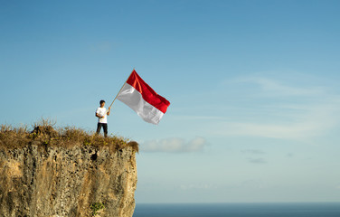 Fototapeta na wymiar proud indonesian man on a beach cliff raising red and white indonesia flag