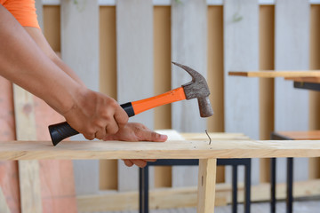 carpenter using the hammer hit a nail for assembly wood.