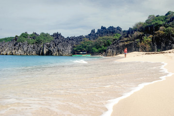 A girl walking along a tropical sandy beach with crystal clear sea on a sunny day. Rocks and tropical beach. Rocks, tropical beach, summertime in Caramoan Island, Philippines, Asia.