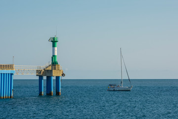 Fototapeta na wymiar Green Lighthouse with sailing yacht at the Entrance to the marina. Seascape.