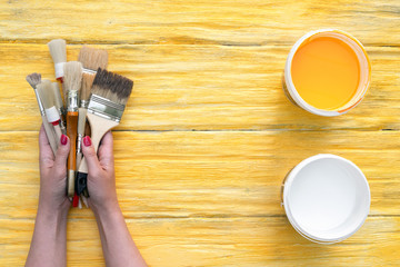 Paintbrushes in a hands and a cans of paint on a yellow board background with a copy space.