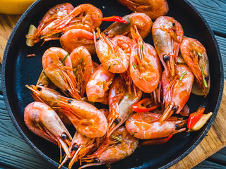 Fried prawns with hot peppers in a frying pan on a wooden board. Table setting