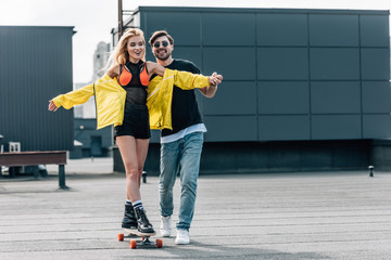 attractive and smiling woman skateboarding and man in glasses hugging her