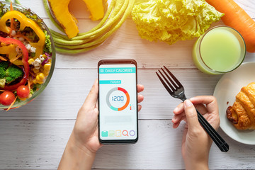 Calories counting , diet , food control and weight loss concept. woman using Calorie counter application on her smartphone at dining table with salad, fruit juice, bread and vegetable - obrazy, fototapety, plakaty
