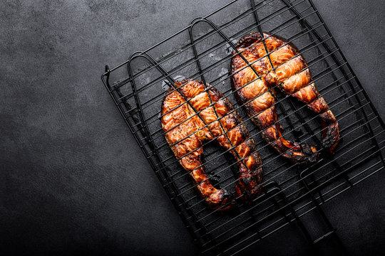 Grilled salmon on iron grill grate on a dark background top view. BBQ seafood. spece for a text
